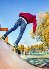 Skateboarder jumping in city skatepark at the halfpipe in the autumn day