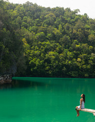 Fototapeta na wymiar A woman sitting on the edge of a diving board in a magnificent green lagoon.