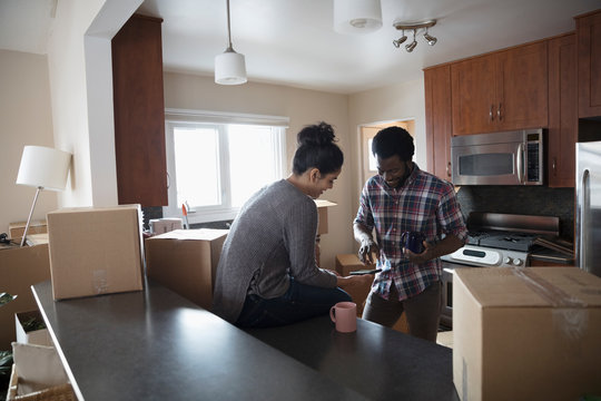 Young couple moving into new house, taking coffee break and using smart phones in kitchen