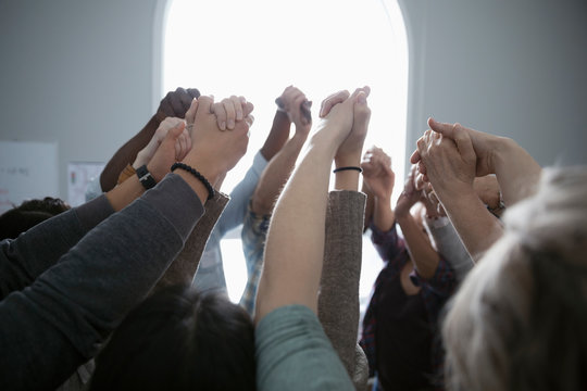 Support group holding hands overhead in huddle, in support