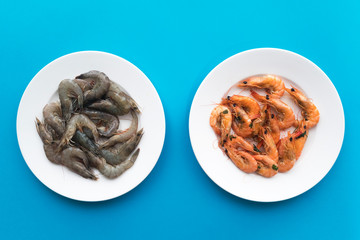 Seafood, cooked, boiled or fried shrimps and raw uncooked shrimps, king tiger prawns on blue background in white plates. Top view. Healthy protein food, diet. Comparison. Before and after cooking.
