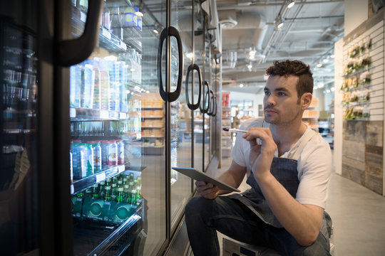 Male worker with digital tablet taking inventory at refrigerated case in grocery store