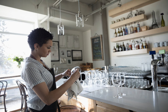 Young Woman Small Business Owner Drying Wine Glasses In Bar