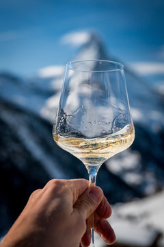 hand holding a glass of white wine in front of Matterhorn in winter in a Restaurant