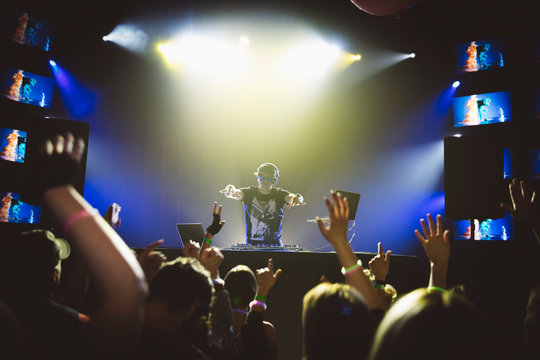 DJ on stage gesturing to crowd dancing in nightclub