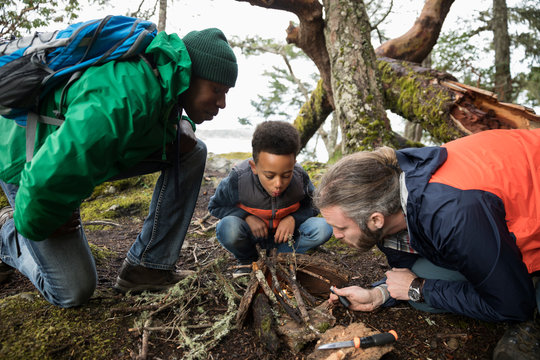 Trail guide teaching father and son how to build campfire in woods