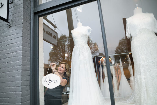Bridal boutique owner hanging open sign in window