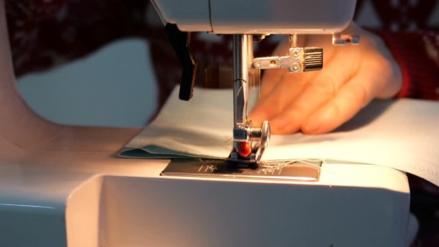 Tailoring Process - Womens hands using sewing machine with light of built-in lamp, that would making textile clothes. Needle with looper and presser foot. Handcraft concept.