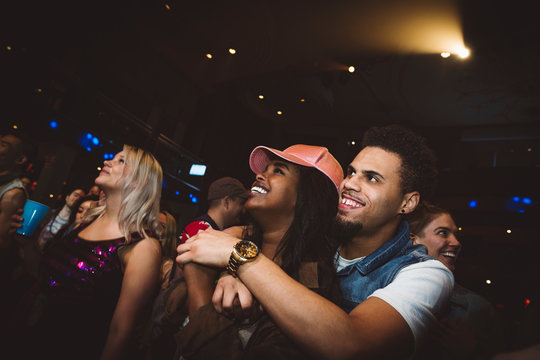 Happy young millennial couple hugging, enjoying music concert at nightclub