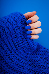 Blue matte manicure on a blue background with round blue glasses. 