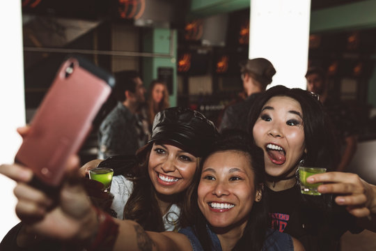 Playful, Exuberant Young Female Millennial Friends Taking Shots And Taking Selfie In Nightclub