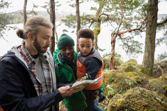 Trail Guide Showing Plant And Guidebook To Curious Father And Son Hiking In Woods