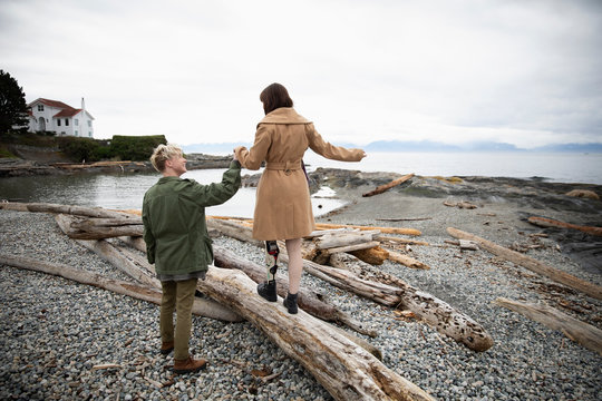 Young man holding hands with amputee girlfriend walking on beach driftwood