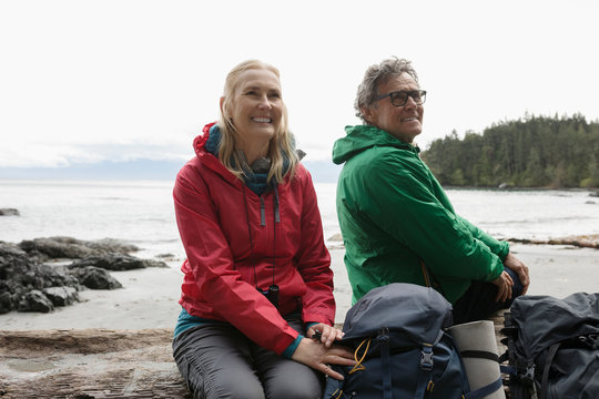 Carefree Active Senior Couple Backpacking, Resting On Rugged Beach