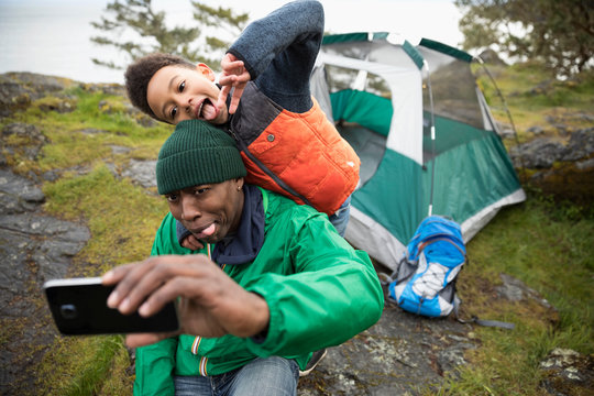 Playful father and son making faces, taking selfie at campsite