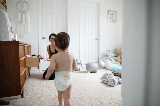 Mother Watching Baby Son In Diaper Walking In Nursery