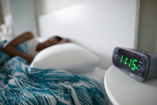 Alarm clock on bedside table next to teenage girl sleeping in
