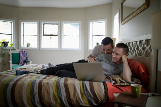 Male gay couple relaxing, using laptop on bed