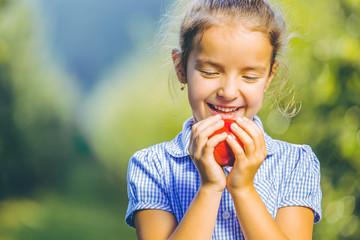 Cropped portrait of hungry female kid is ready to taste an autumnal apple, enjoying annual harvest in apple-trees garden.