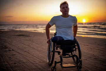 Handicapped man in wheelchair and his girlfriend alone on a beach at sunset