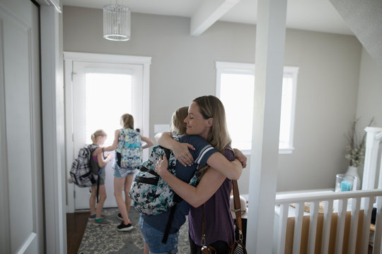 Affectionate mother hugging tween schoolgirl daughter with backpack in foyer