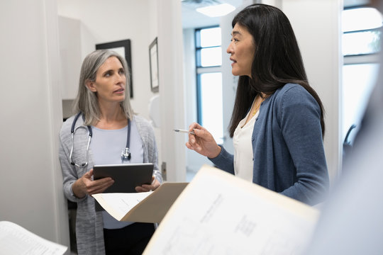 Female Doctors Discussing Medical Record In Clinic Corridor