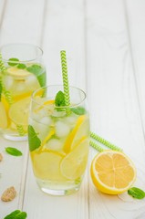 Homemade lemonade with lemon slices, mint and brown sugar in a glass with ice on a white wooden background. Vertical orientation.