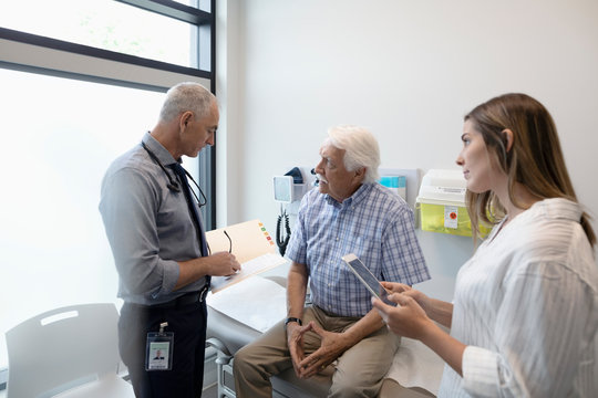 Male doctor discussing medical record with senior patient in clinic exam room