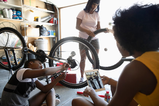 Mother and tween daughters with digital tablet fixing bicycle in garage