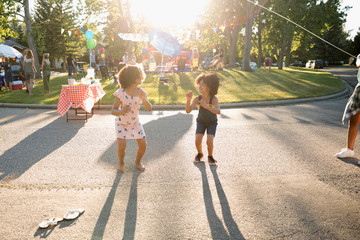 Cute sisters jump roping at summer neighborhood block party in sunny street