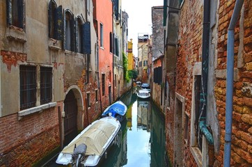 quiet narrow Venetian canal, with boats located between the old houses