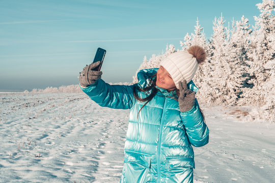 teen girl take a selfie on a sunny winter day and smiling. Girl is showing victory sign with her fingers