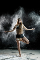 Beautiful girl model on a black background throws flour