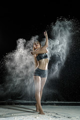 Fototapeta na wymiar Beautiful girl model on a black background throws flour