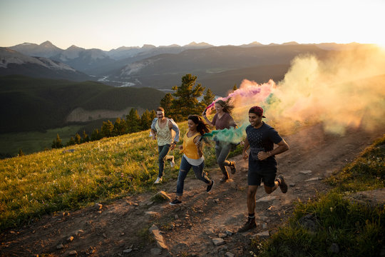 Playful friends enjoying colorful smoke bombs on sunny mountain road, Alberta, Canada
