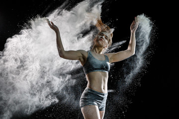 Beautiful girl model on a black background throws flour