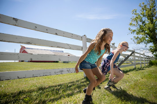 Playful sisters jumping off fence at sunny rural farm