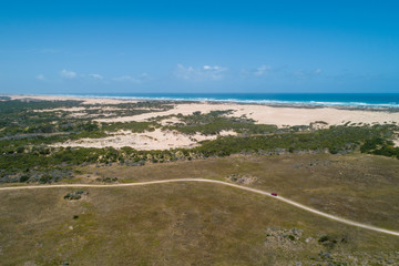 Red car on unsealed road near the ocean under blue sky - aerial view