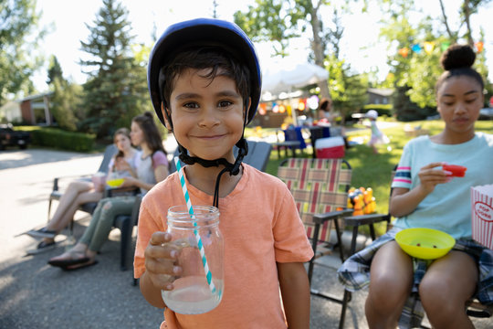 Portrait cute boy in bike helmet drinking lemonade at summer neighborhood block party in park