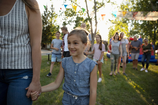 Smiling girl holding hands with mother at summer neighborhood block party in park