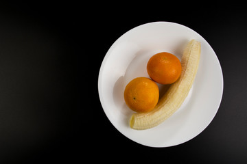 Peeled banana and two mandarines lie on a plate