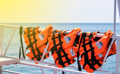Orange life jacket is a safety device hanging on a steel railings.