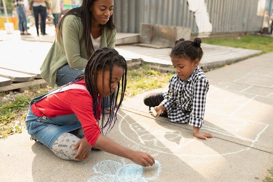 Mother and daughters drawing with sidewalk chalk
