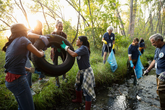 People volunteering, cleaning up garbage and tire in stream