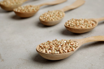 Uncooked green buckwheat grains in spoons on light table
