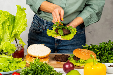 Girl puts a leaf of lettuce on the fried cutlet. Making a burger.