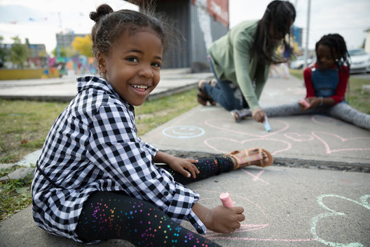Portrait smiling, cute girl drawing with sidewalk chalk