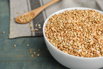 Uncooked green buckwheat grains in bowl on light blue wooden table, closeup