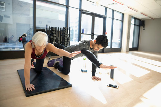 Personal trainer guiding senior woman doing balance stretch in gym studio