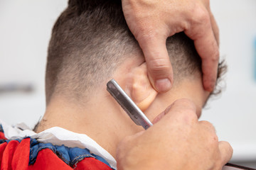 The hairdresser cuts the boy's hair with a razor